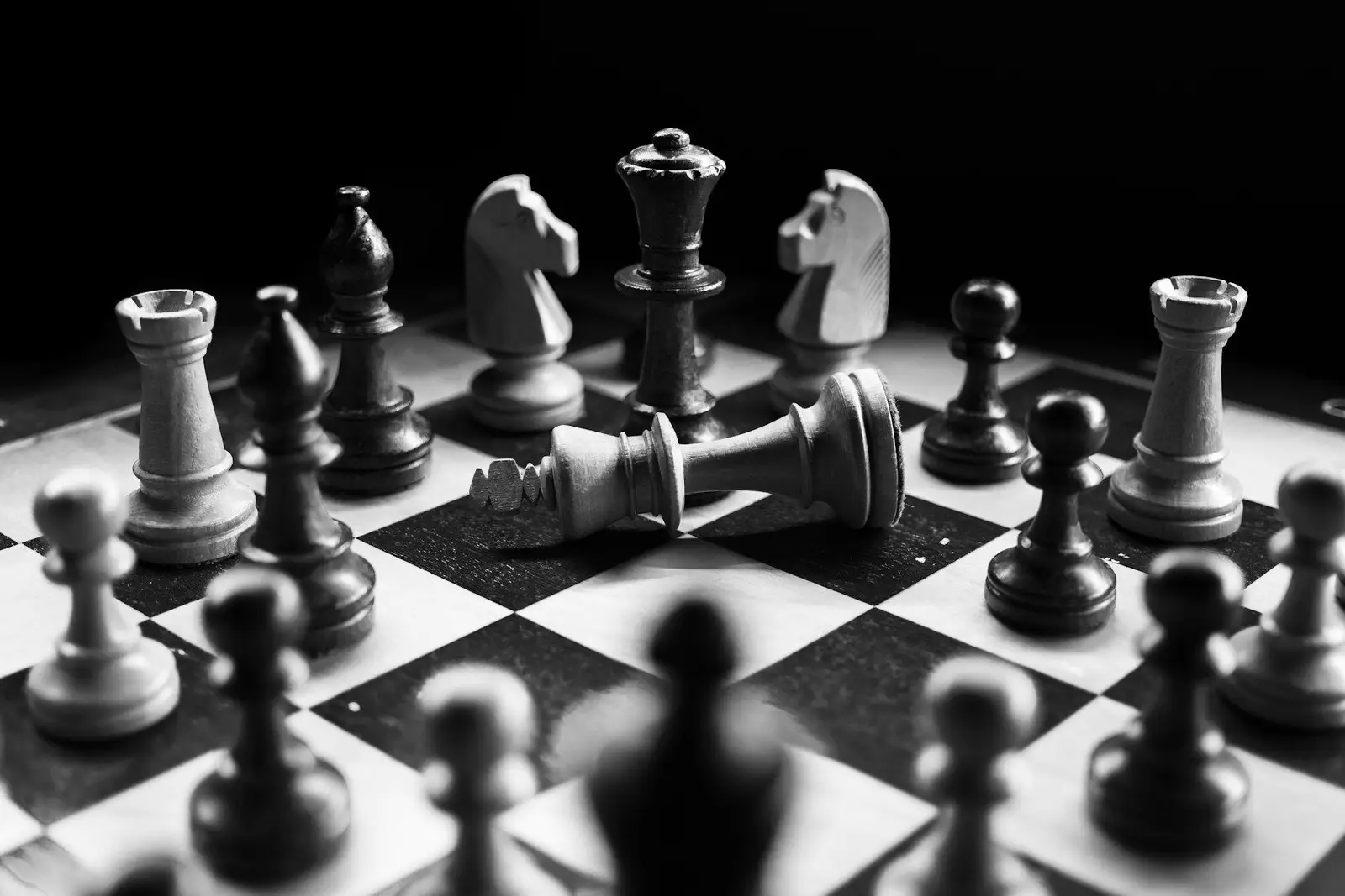 Black and white chess board mid-game with a toppled piece in the foreground